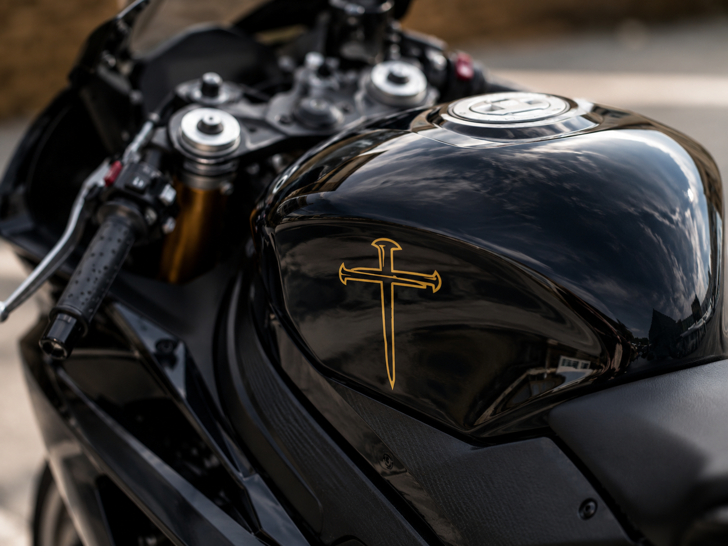 Gold outline nail cross vinyl decal on black motorcycle tank