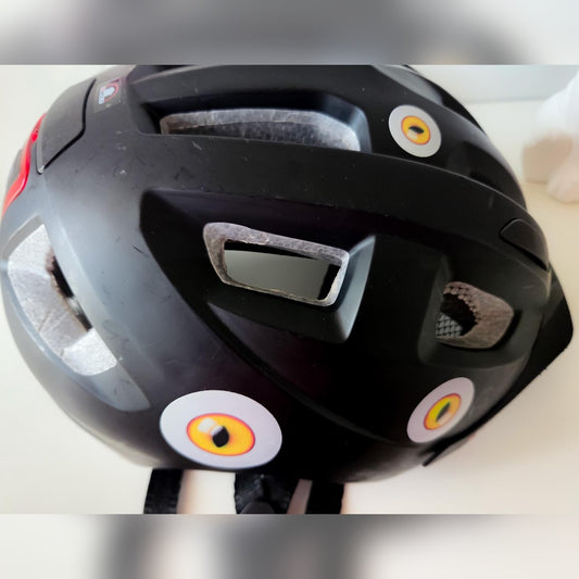 Anti-swooping bird deterrent decal – three cat-eye stickers on the shell of a black bike helmet