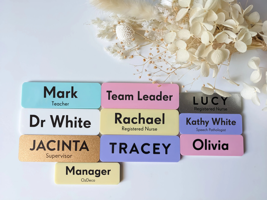Colorful name tags with various names and titles on a light background with flowers.