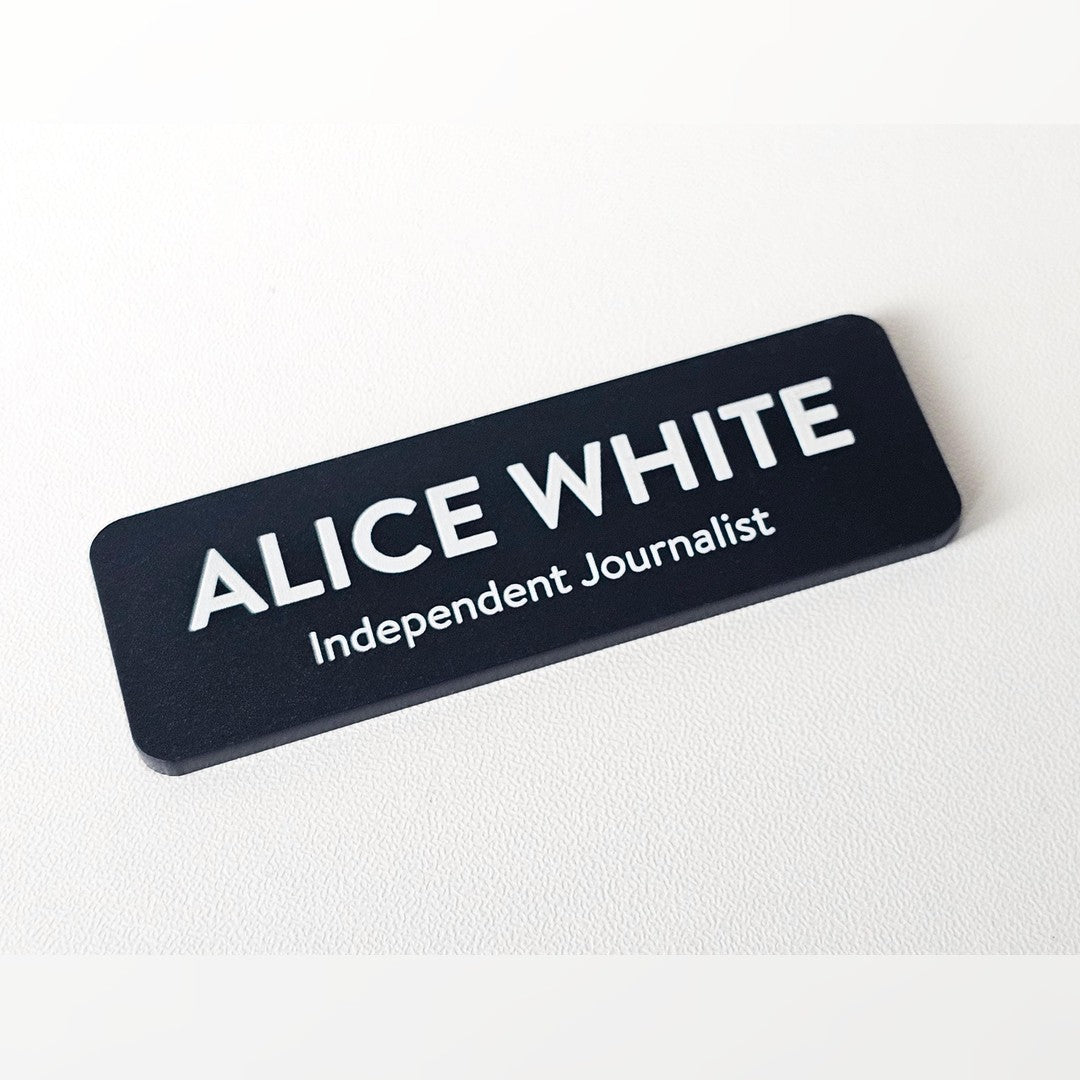 Acrylic name badge – black matte badge with white name ALICE WHITE and Independent Journalist line, on a white surface