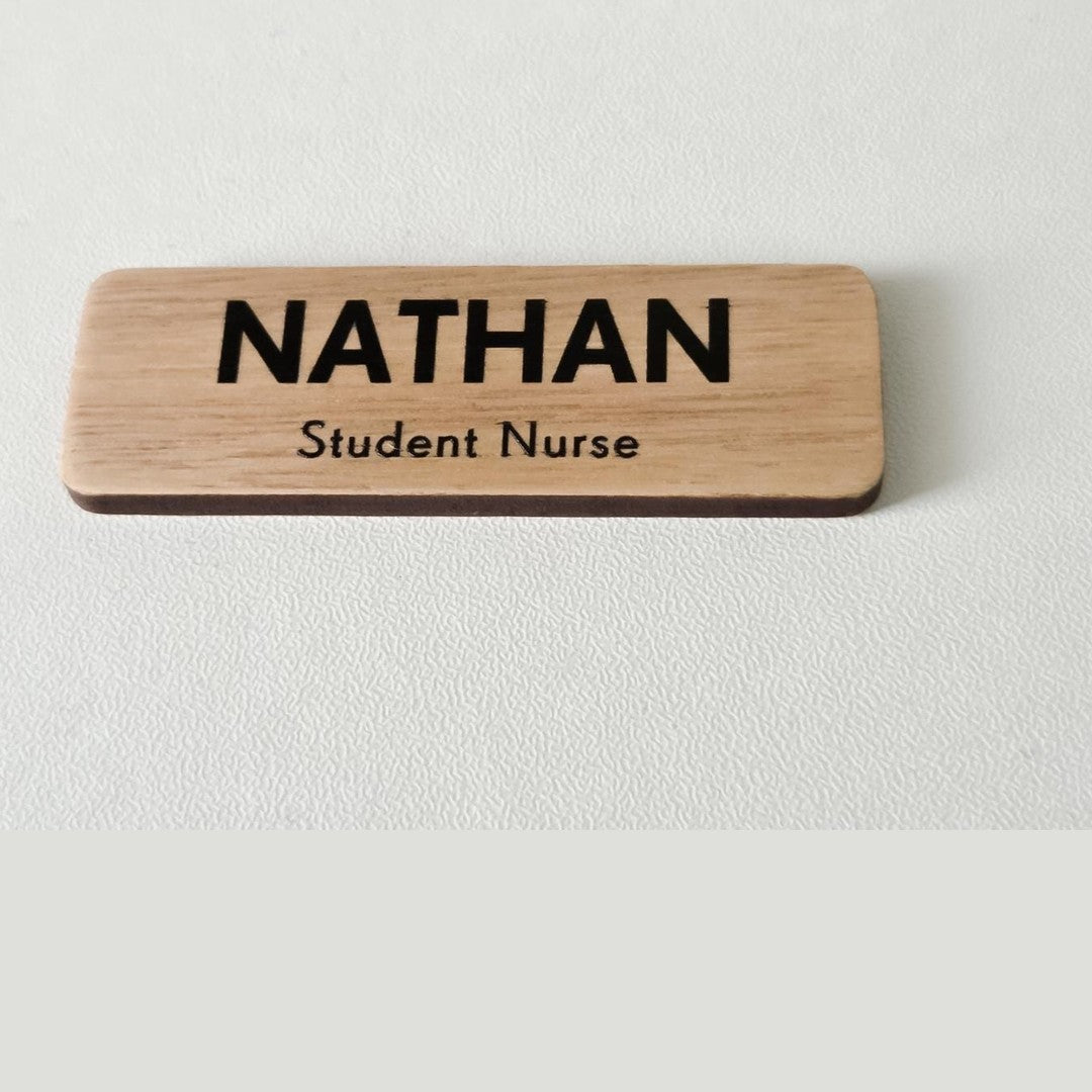 Wooden name badge – black name NATHAN with Student Nurse line below on a pale timber badge, on a white surface