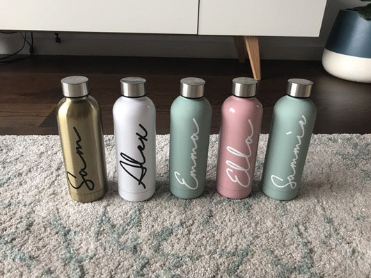 Personalised vinyl name decals on five insulated drink bottles in gold, white, sage, pink and mint, each with a name in script lettering