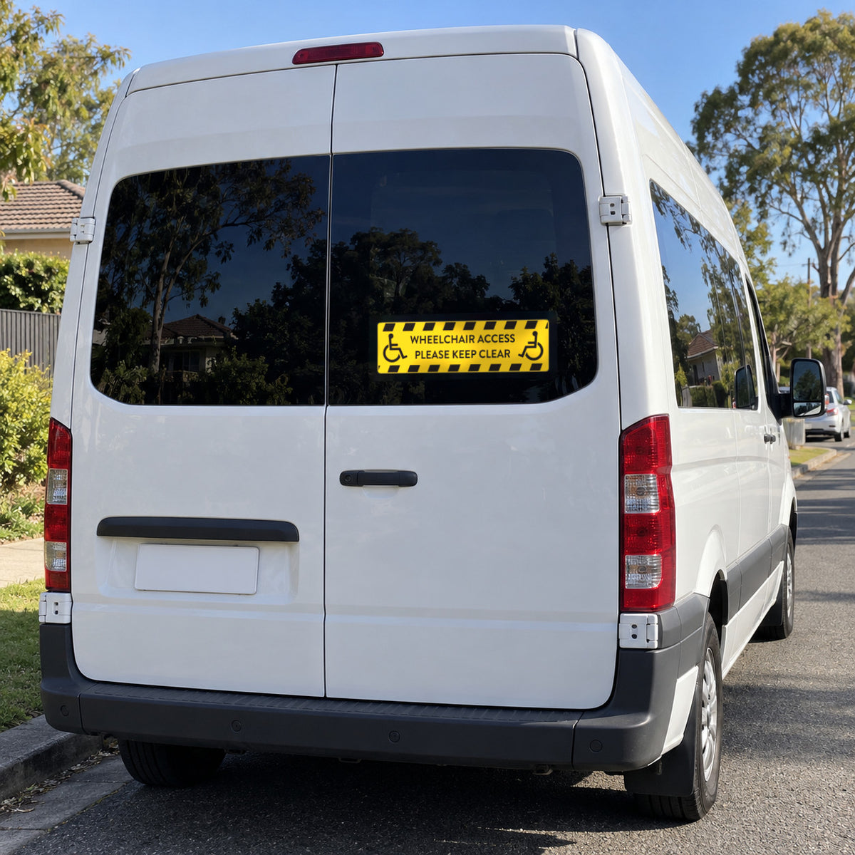 Option 1 yellow wheelchair access decal with black hazard stripes and two wheelchair symbols, reading WHEELCHAIR ACCESS, PLEASE KEEP CLEAR, applied to the rear door window of a white wheelchair-accessible van.