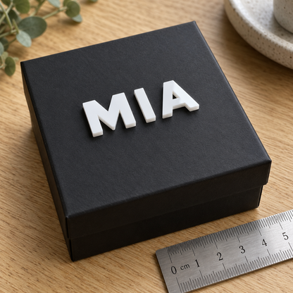 Small white gloss acrylic letters 'MIA' on a black gift box beside a ruler