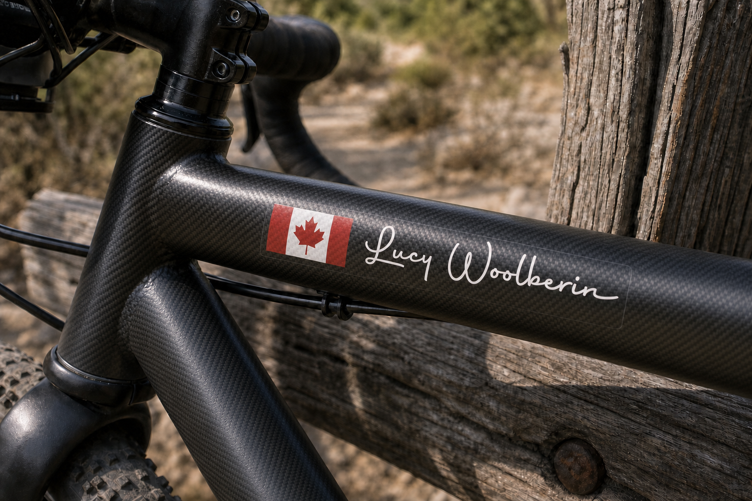 Custom flag and name sticker in handwritten script with white lettering on a carbon bicycle frame, with Canadian flag