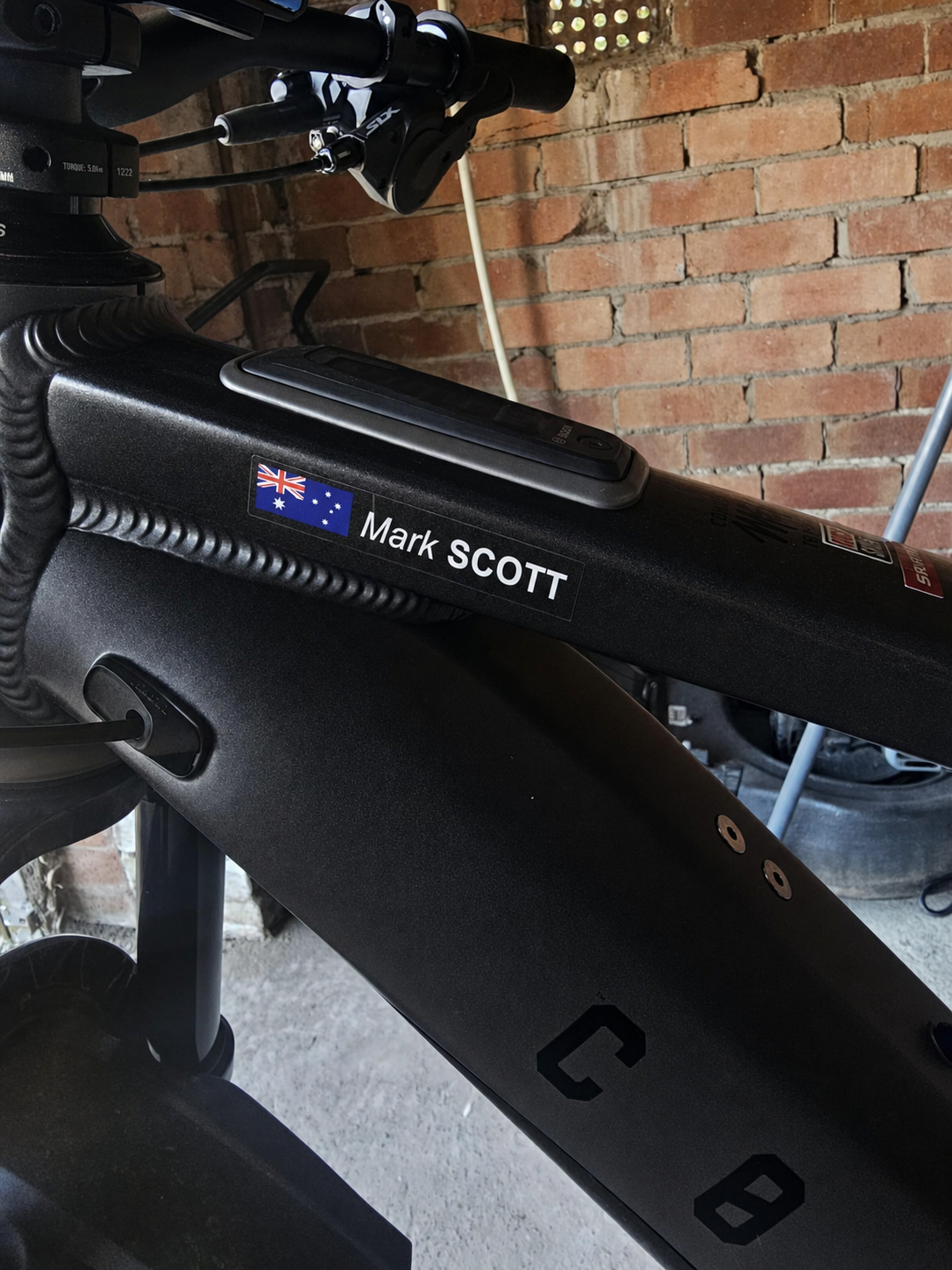 Custom flag and name sticker with a light first name and bold capital surname in white on a black bicycle frame, with Australian flag