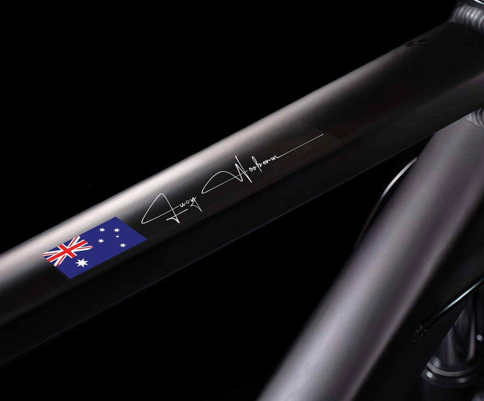 Custom flag and name sticker in signature script applied to a black bicycle top tube, with Australian flag